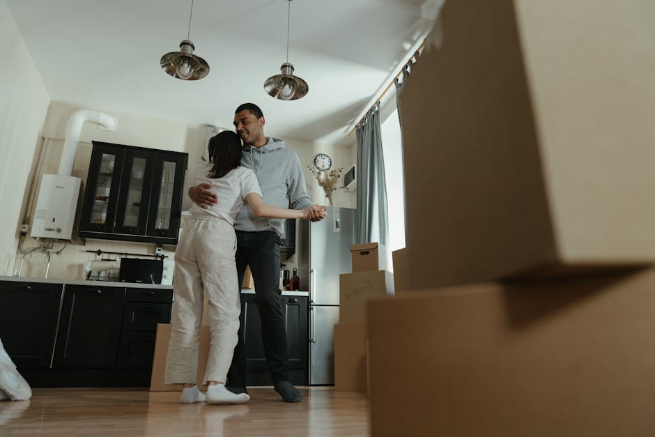 Inside a residential property during a home relocation, a woman is seated on the floor near a partially covered window with plastic sheeting, appearing to be organizing or packing. In the background,